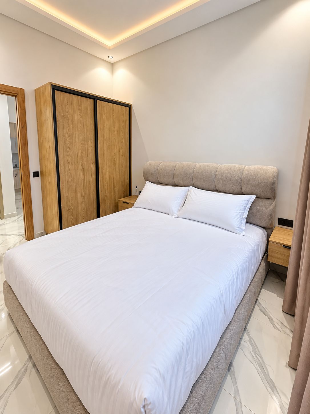 A modern bedroom with a large bed, wooden wardrobe, and a nightstand.