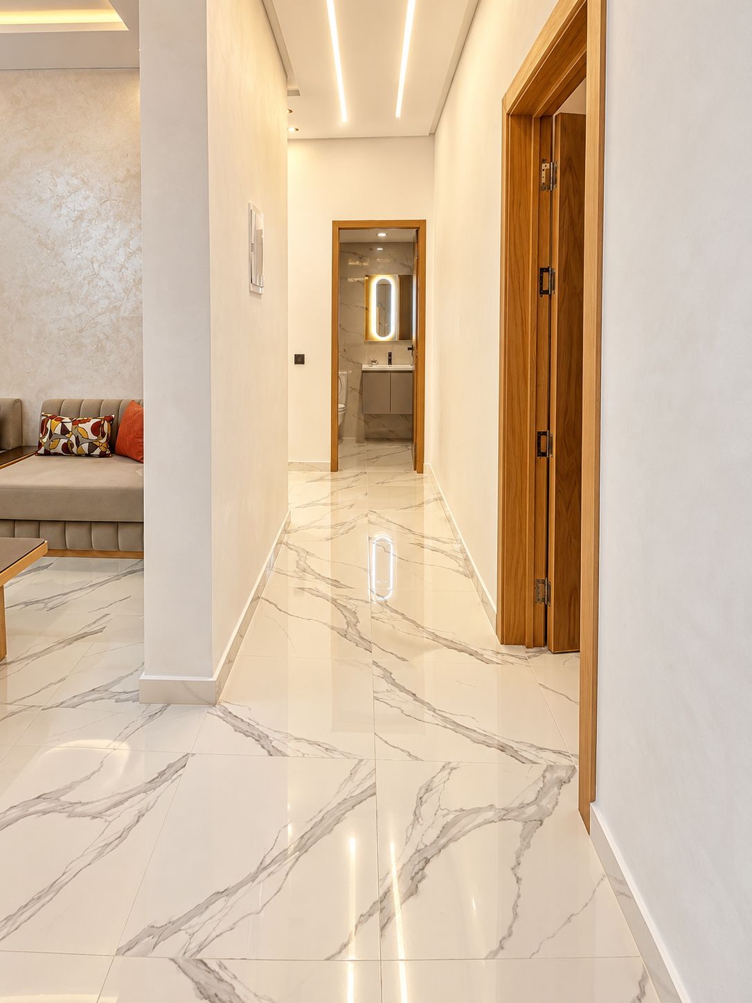 A hallway with a marble floor, a wooden door, and a bathroom visible in the distance.