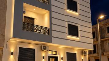 A modern two-story building with balconies, a central entrance, and outdoor lighting.