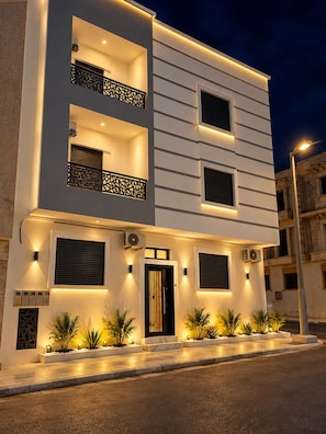A modern two-story building with balconies, a central entrance, and outdoor lighting.
