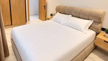 A modern bedroom with a large bed, a wooden wardrobe, and a nightstand with a plant.