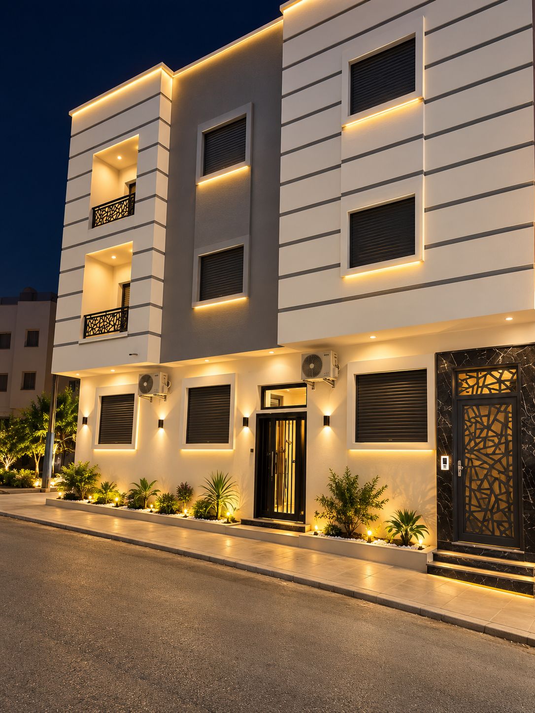 A modern multi-story building with balconies, a central entrance, and outdoor lighting.