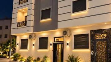A modern multi-story building with balconies, a central entrance, and outdoor lighting.