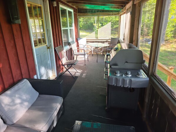 A covered porch with a grill, seating area, and a view of the outdoors. - Rustic Antigonish Cabin Retreat (Antigonish)
