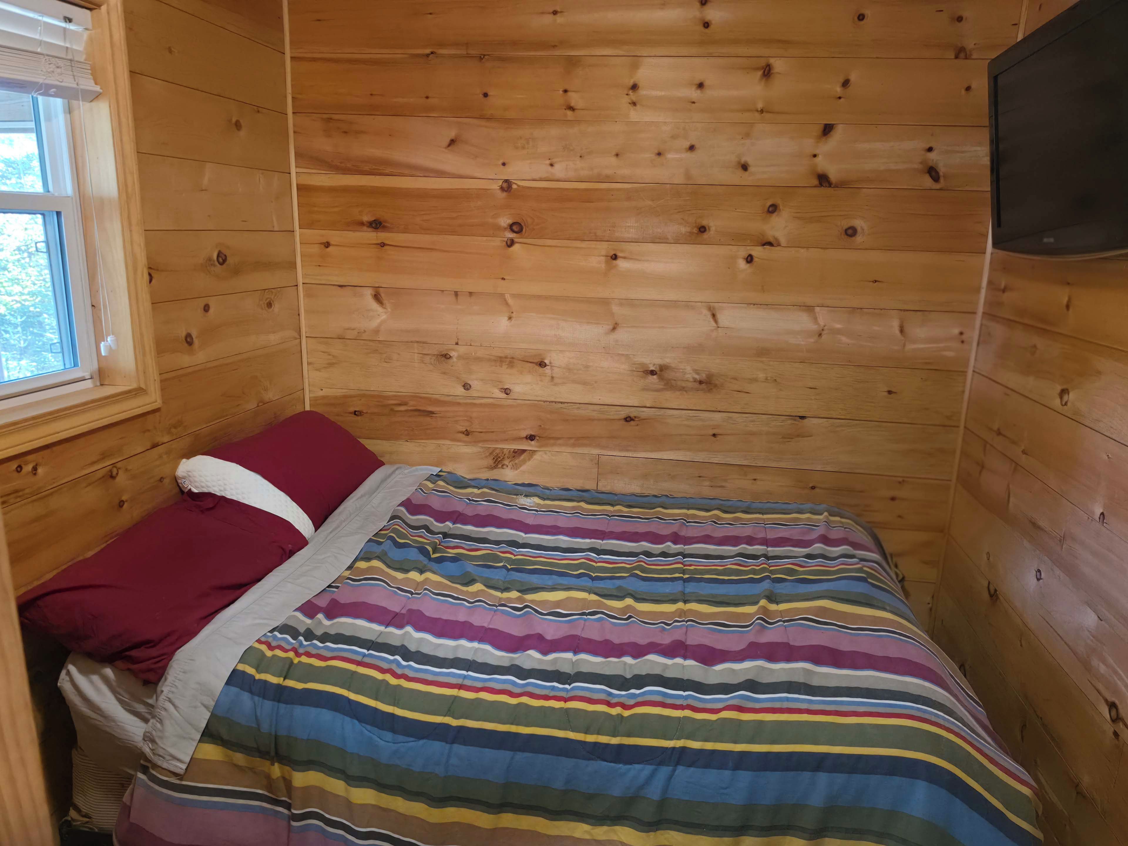 Puupaneloitu huone, jossa on sänky, ikkuna ja televisio.