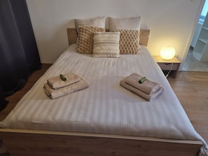 Ein ordentlich bezogenes Bett mit Kopfstütze, Kissen und zwei gefalteten Handtüchern mit Flaschen darauf.