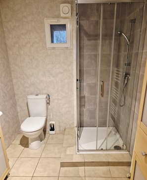 Ein Badezimmer mit Toilette, Duschkabine und einem kleinen Fenster über der Toilette.