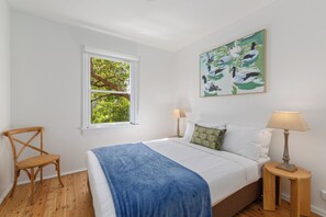 A bedroom with a bed, a window, a chair, a lamp, and a painting on the wall. - Harbourside Life Scenic Walks and Vibrant Nightlife (Darlinghurst)