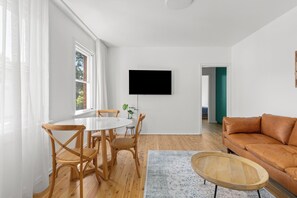 Ein modernes Wohnzimmer mit Essbereich, Holzboden, einem flachbildfernseher an der Wand und einem braunen Ledersofa.