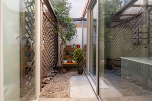 Um espaço exterior estreito com cerca de madeira, plantas em vasos e uma pequena mesa.