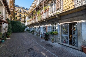 Ein Innenhof mit einem Kopfsteinpflasterweg, Blumentöpfen und einem Gebäude mit mehreren Balkonen.