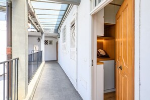 Un couloir étroit, doté d’une rambarde métallique, d’une porte en bois et d’une fenêtre donnant sur le ciel.