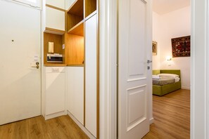 A hotel room with a wooden floor, a bed with a green headboard, a small sitting area with a green sofa, and a wooden cabinet with a telephone and a small mirror. - Palazzo De Sangro a Spaccanapoli, 3 camere (Naples)