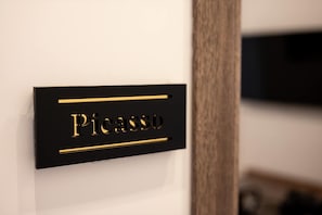 A black sign with gold lettering spelling 'Picasso' on a white wall. - Picasso - The President, Stanza con un l · The President, Stanza con un letto picasso (Naples)