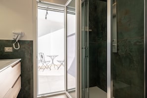 A bathroom with a glass shower door, a hairdryer on the wall, and a view of an outdoor seating area. - Picasso - The President, Stanza con un l · The President, Stanza con un letto picasso (Naples)