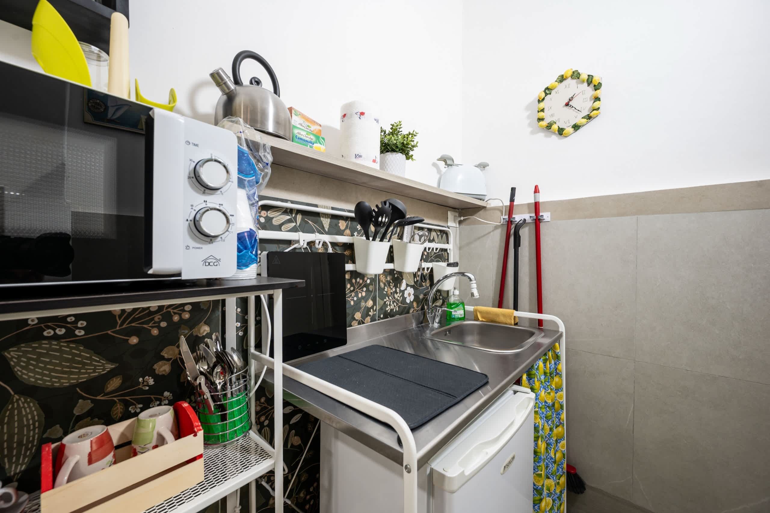 A kitchen with a microwave, kettle, and a clock on the wall.