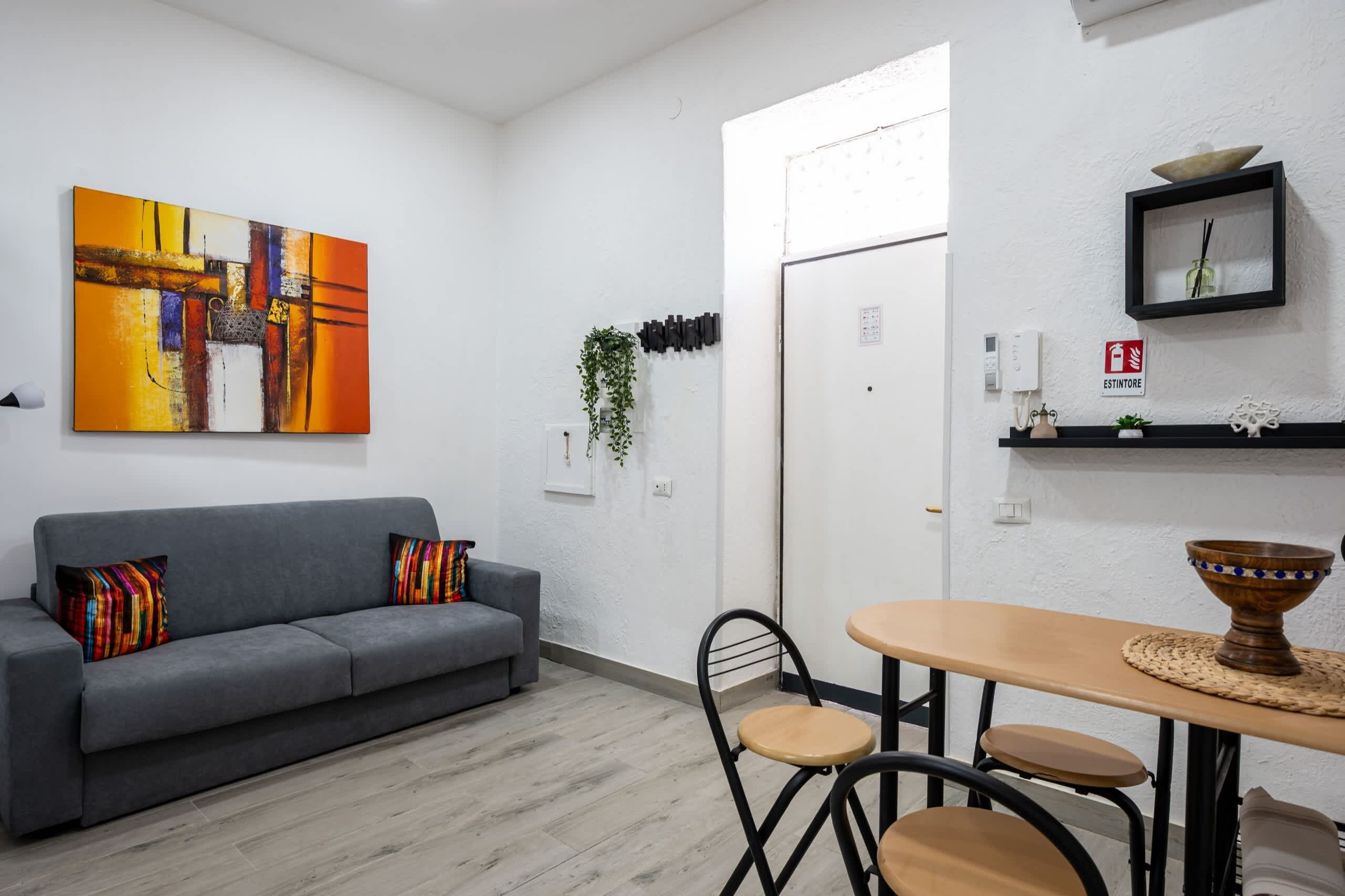 A modern living room with a gray sofa, a vibrant abstract painting, and a dining area with a round table and chairs.