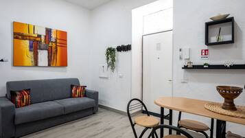 A modern living room with a gray sofa, a vibrant abstract painting, and a dining area with a round table and chairs.
