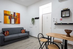 A modern living room with a gray sofa, a vibrant abstract painting, and a dining area with a round table and chairs. - 10 min dall'aeroporto - navetta - self check-in (Naples)