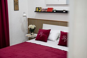 A neatly arranged bedroom with a bed, pillows, a bedside table with a book and a vase of flowers, and a shelf with books and a small plant. - 10 min dall'aeroporto - navetta - self check-in (Naples)