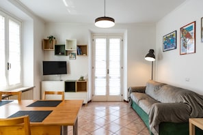 A living room with a wooden dining table, a sofa, a TV, and a lamp. - Attico con terrazzo - 300 m dalla stazione (Varese)