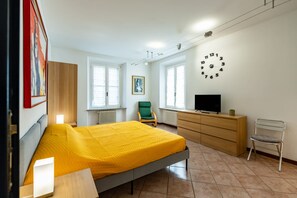 Ein Schlafzimmer mit einem Bett, einem Schminktisch, einem Sessel, einem Fernseher und einer Wanduhr.