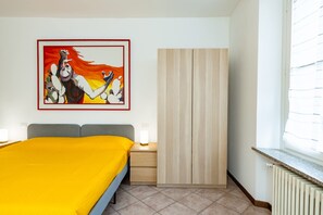 A hotel room with a bed, a wardrobe, a nightstand, a lamp, and a painting on the wall. - Attico con terrazzo - 300 m dalla stazione (Varese)