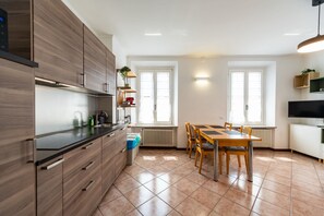 A modern kitchen with wooden cabinets, a dining table with chairs, and a TV on a cabinet. - Attico con terrazzo - 300 m dalla stazione (Varese)