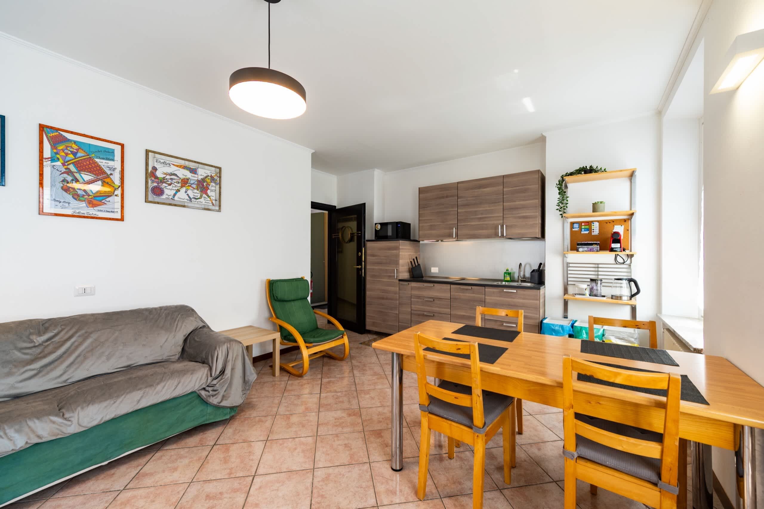 A compact living space with a kitchenette, a dining area with a wooden table and chairs, a green sofa, and a ceiling light fixture.