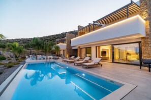 A modern poolside area with a clear pool, lounge chairs, and a stone building with large windows. - Three Bedroom Villa in Nafplio (Nafplio)