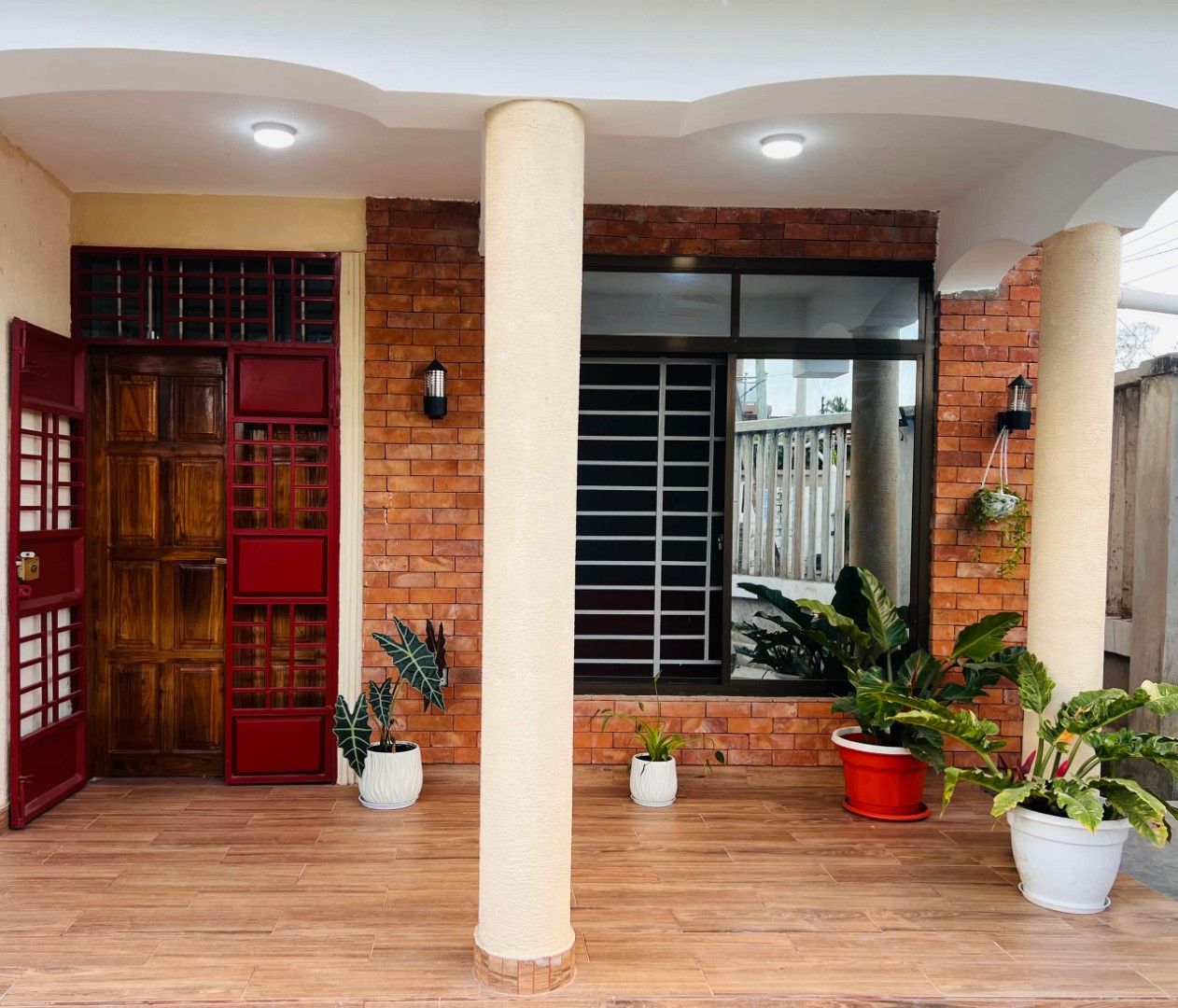 Una entrada techada con puerta de madera, paredes de ladrillo y plantas en macetas.