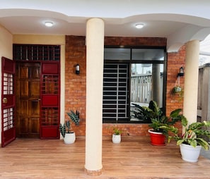 Una entrada techada con puerta de madera, paredes de ladrillo y plantas en macetas.