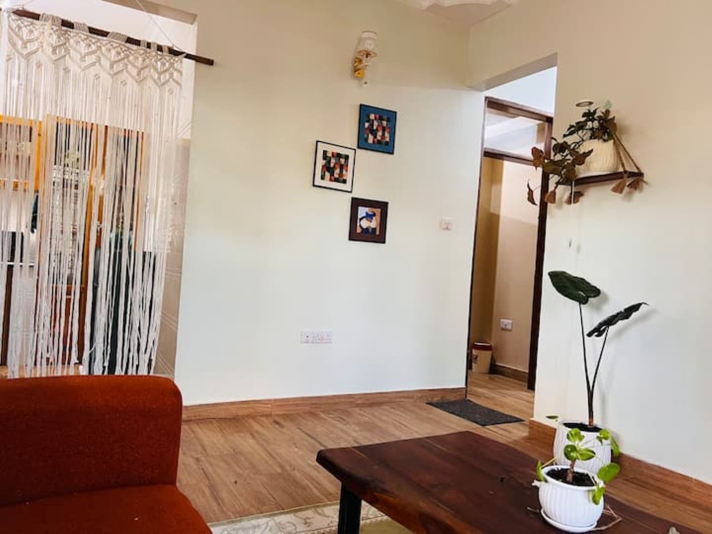 Una sala de estar con un sofá, una mesa de centro y dos plantas en macetas. Hay dos cuadros colgados en la pared.