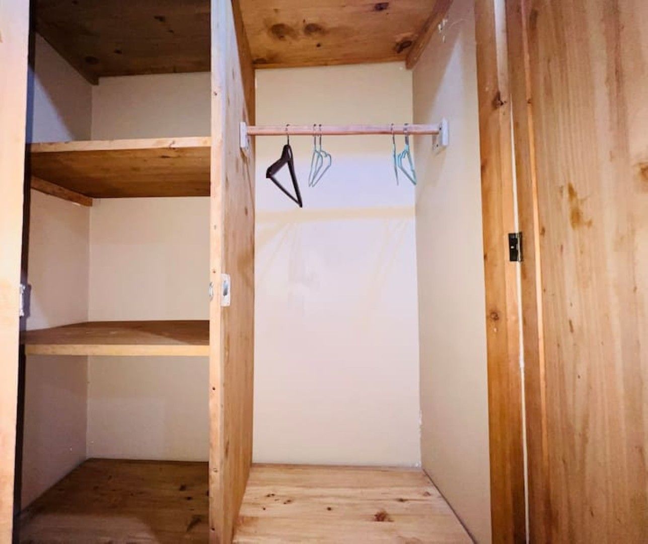 Un armario de madera con una barra metálica y ganchos para colgar objetos.