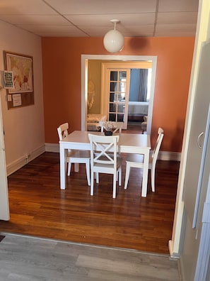 A dining area with a table and chairs, a hanging light fixture, and a view into a bedroom through a doorway.