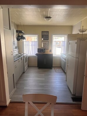 A compact kitchen with a microwave, stove, and refrigerator. There is a chair in the foreground, and the room has a simple, functional design. - Winona's Inn / Historic Downtown Hillsdale / Sleeps 9 / Hillsdale College (Hillsdale, MI)