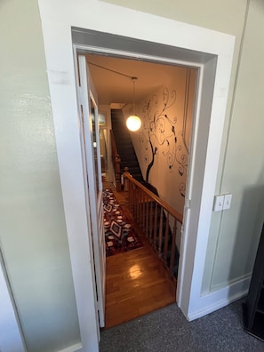 A hallway with a wooden staircase, a patterned carpet, and a wall with a tree design.