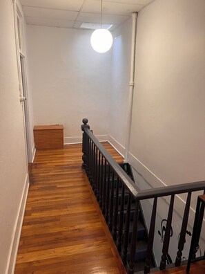 A wooden staircase with a black railing, white walls, and a light fixture. - Winona's Inn / Historic Downtown Hillsdale / Sleeps 9 / Hillsdale College (Hillsdale, MI)