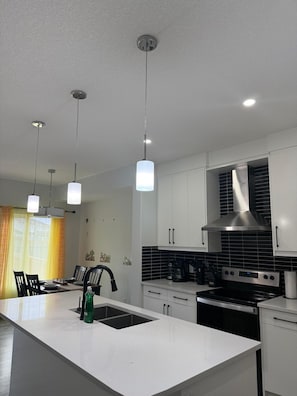 A modern kitchen with white cabinetry, a central island with a sink, and a stainless steel range hood. - Spacious 3BR Duplex Near Edmonton Airport (Edmonton)