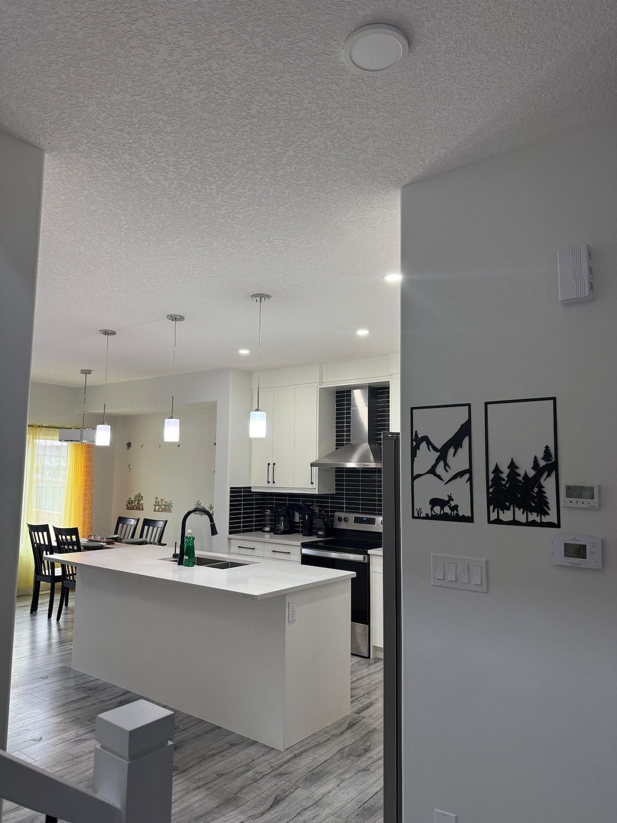 A modern kitchen with a central island, pendant lighting, and a dining area with chairs.