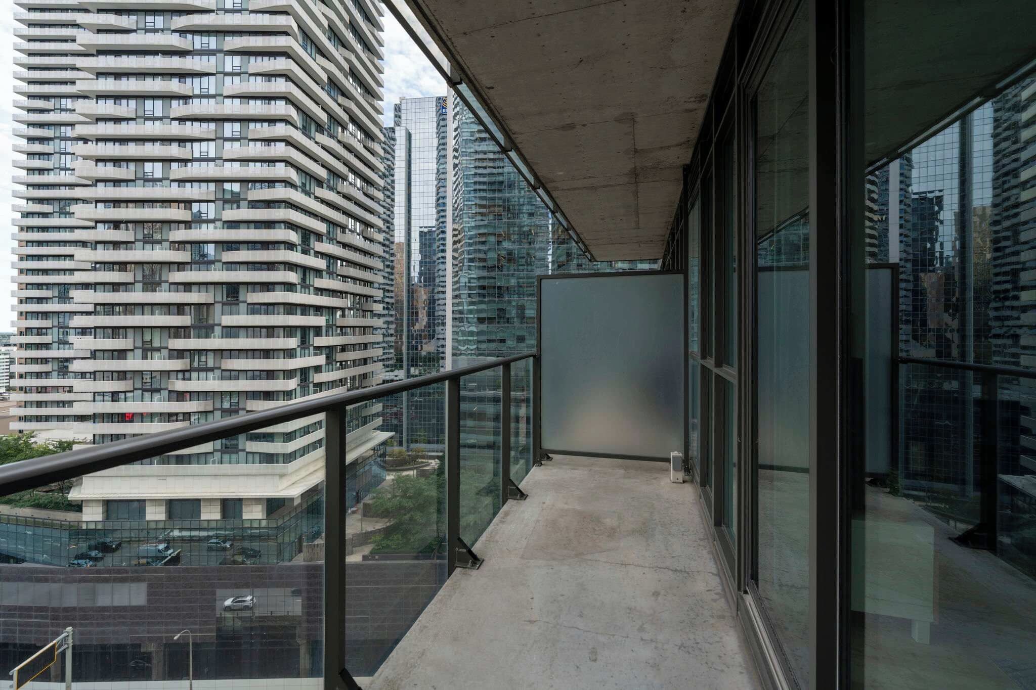 Un balcón con barandilla de vidrio que ofrece vistas a un paisaje urbano con edificios modernos.