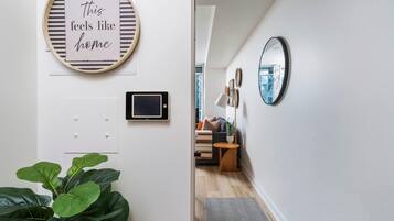 Een hal met een plant, een bord met de tekst 'this feels like home', een wandlamp en een spiegel die op een stadsgezicht reflecteert.