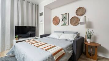 A modern bedroom with a bed, a TV, and a bedside table with a lamp.
