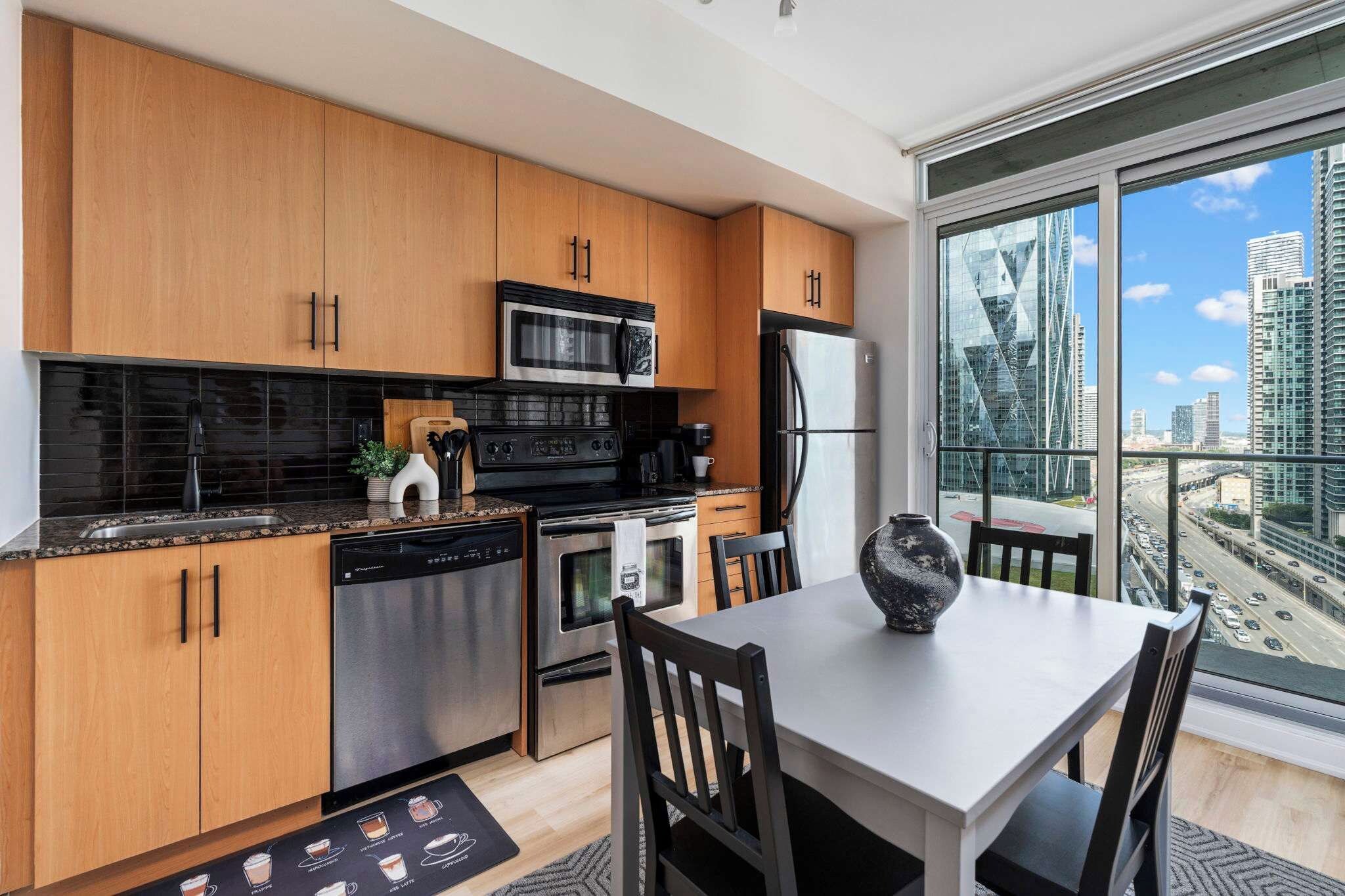 A modern kitchen with wooden cabinets, stainless steel appliances, and a dining area with a view of the city.