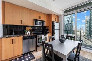 A modern kitchen with wooden cabinets, stainless steel appliances, and a dining area with a view of the city. - City View 1BR - Walk to CN Tower & Union Station (Toronto)