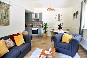 A modern living room with two sofas, a coffee table, and a dining area with a table and chairs. - Kestral Cottage (Brackley)