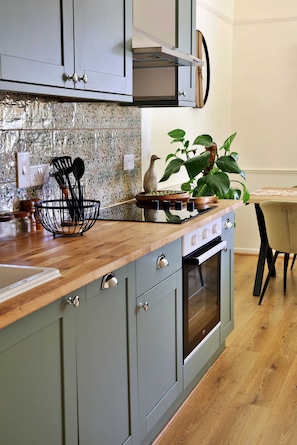 A kitchen with a wooden countertop, a built-in oven, and a backsplash with a textured pattern. - Kestral Cottage (Brackley)