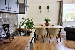 A modern kitchen with a wooden countertop, a dining table with chairs, and hanging plants. - Kestral Cottage (Brackley)