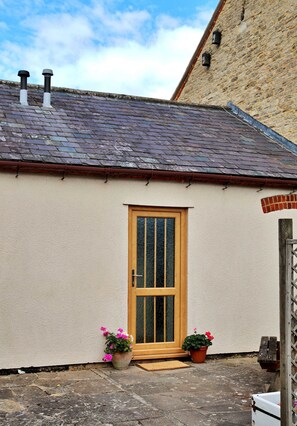 A single-story building with a tiled roof, a wooden door, and two potted plants on the ground. - Kestral Cottage (Brackley)