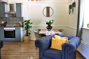 A modern kitchen with a built-in oven and a dining area with a table and chairs. - Kestral Cottage (Brackley)